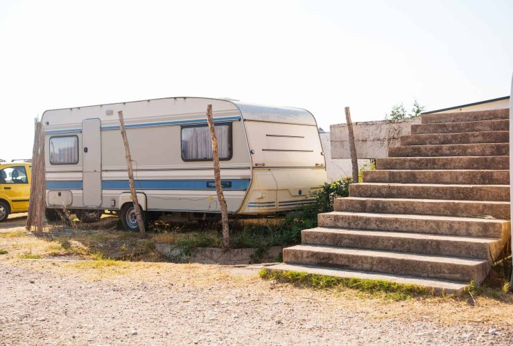 Vintage caravan parked near concrete stairs in outdoor setting, with wooden posts and gravel ground.