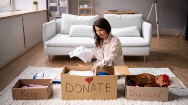 Woman sorting clothes into donation and discard boxes at home.