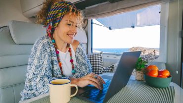 Woman working on a laptop inside a campervan with ocean view.
