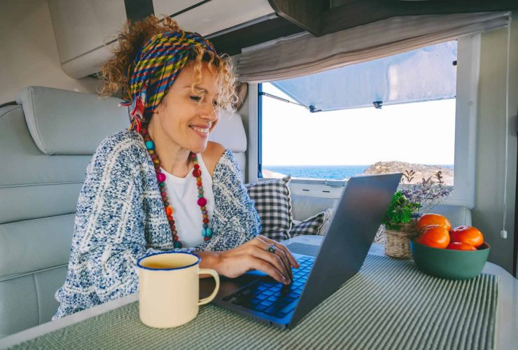 Woman working on a laptop inside a campervan with ocean view.