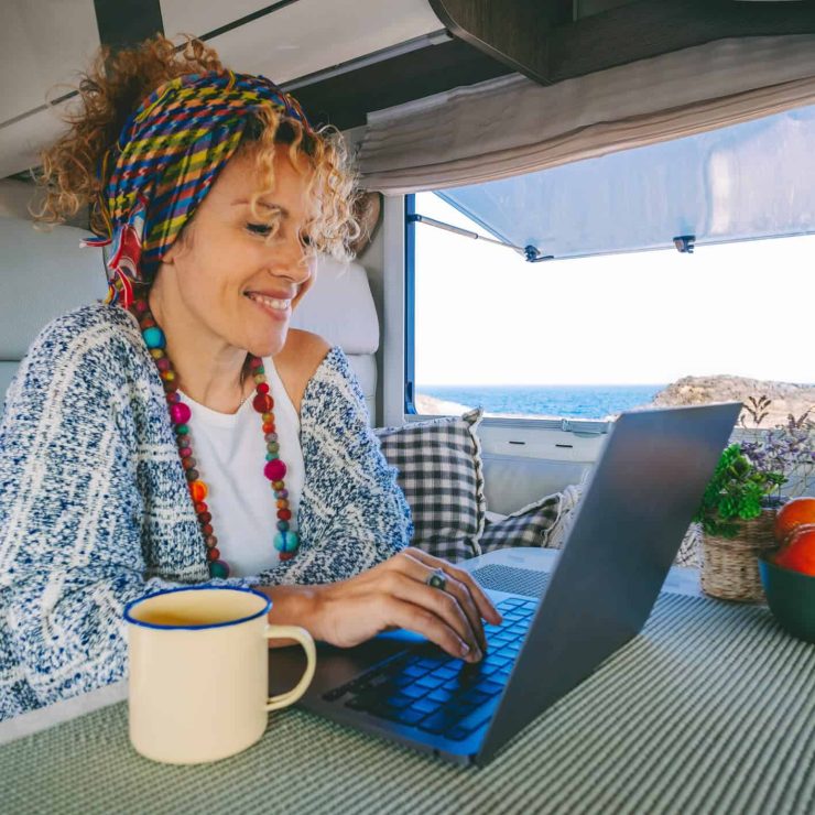 Woman working on a laptop inside a campervan with ocean view.